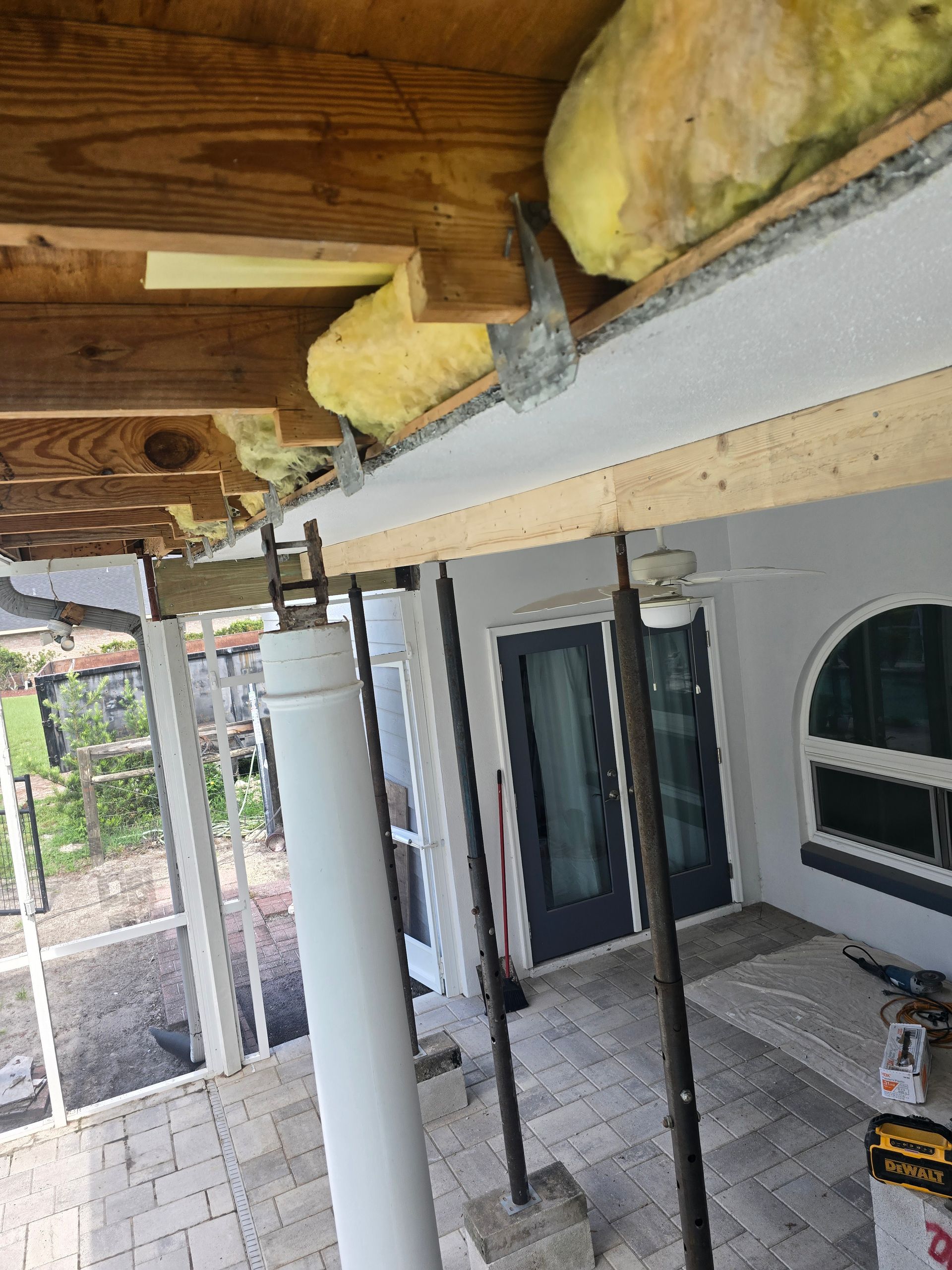 Partially built porch with wooden beams, white column, insulation, and gray siding under construction