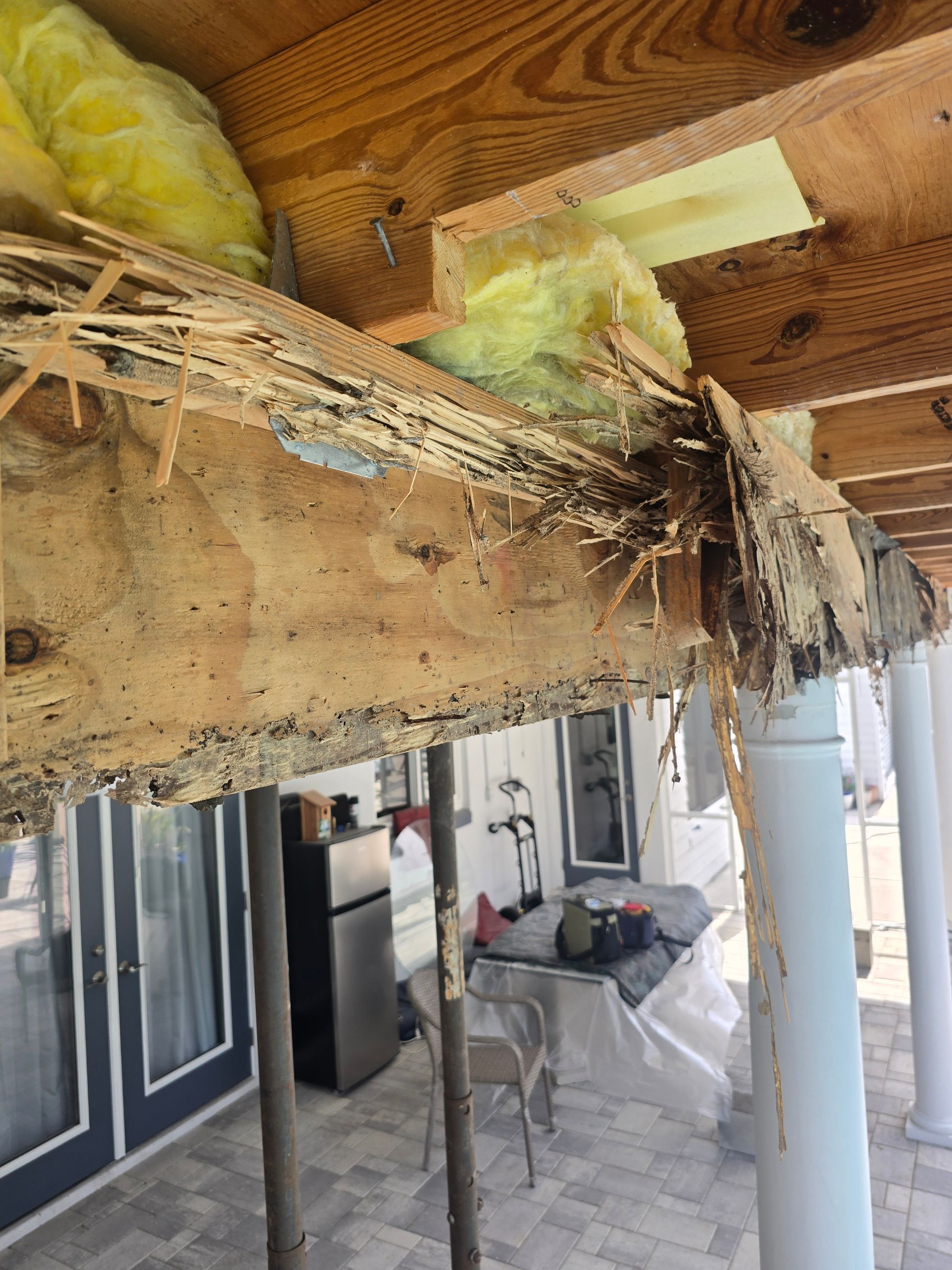 Damaged porch ceiling with exposed wood and insulation above a tiled patio.