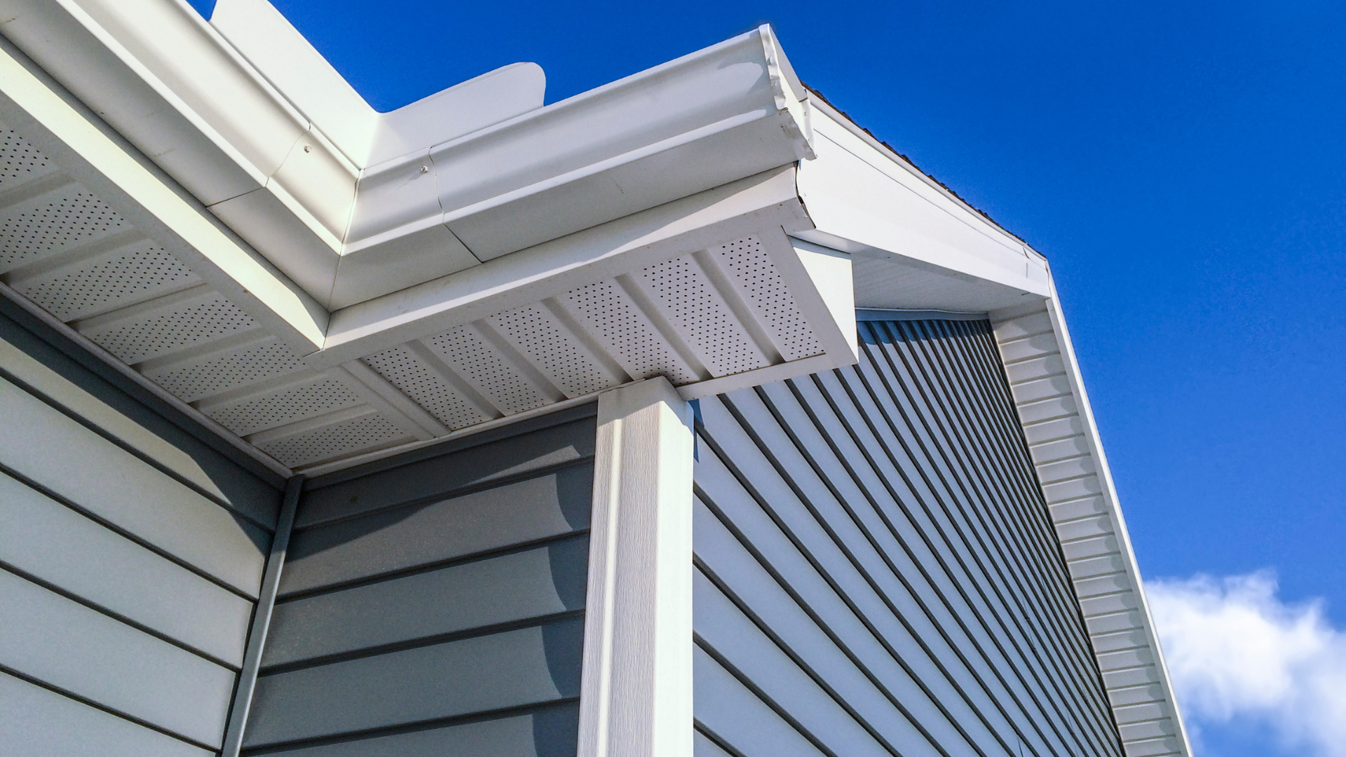 Close-up of white house eaves and blue-gray siding against a clear blue sky
