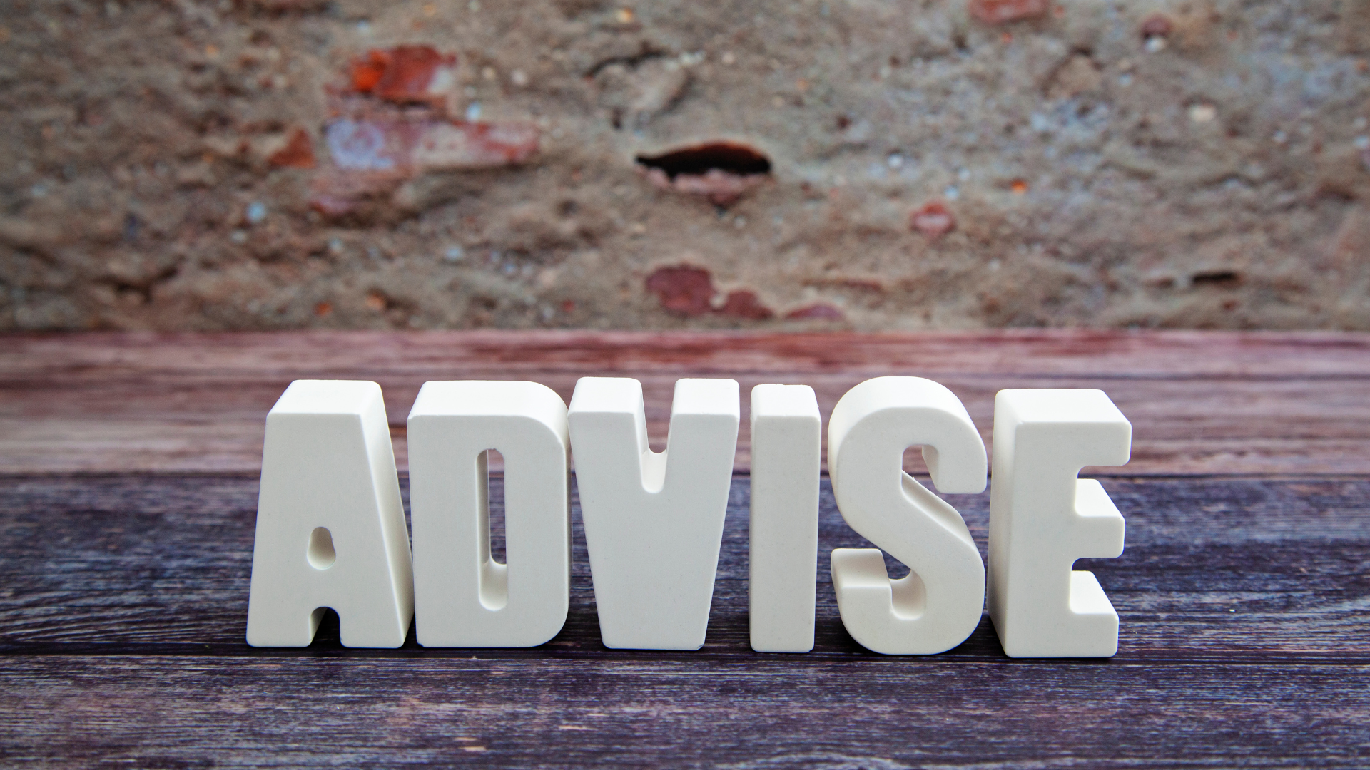 White letters spelling ADVISE on a wooden table, representing business guidance and consulting