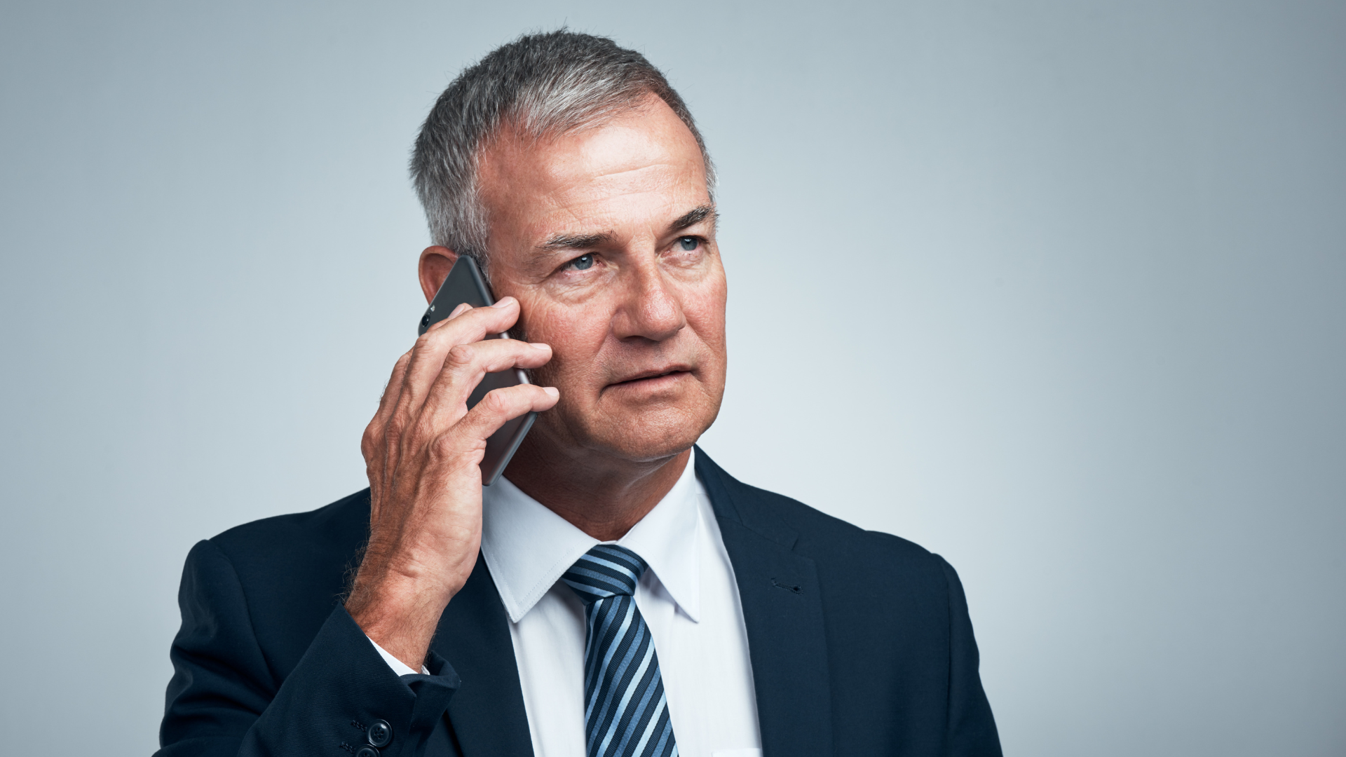 Mature businessman in a navy suit speaking on a smartphone, representing business communication, leadership, and professional decision-making.