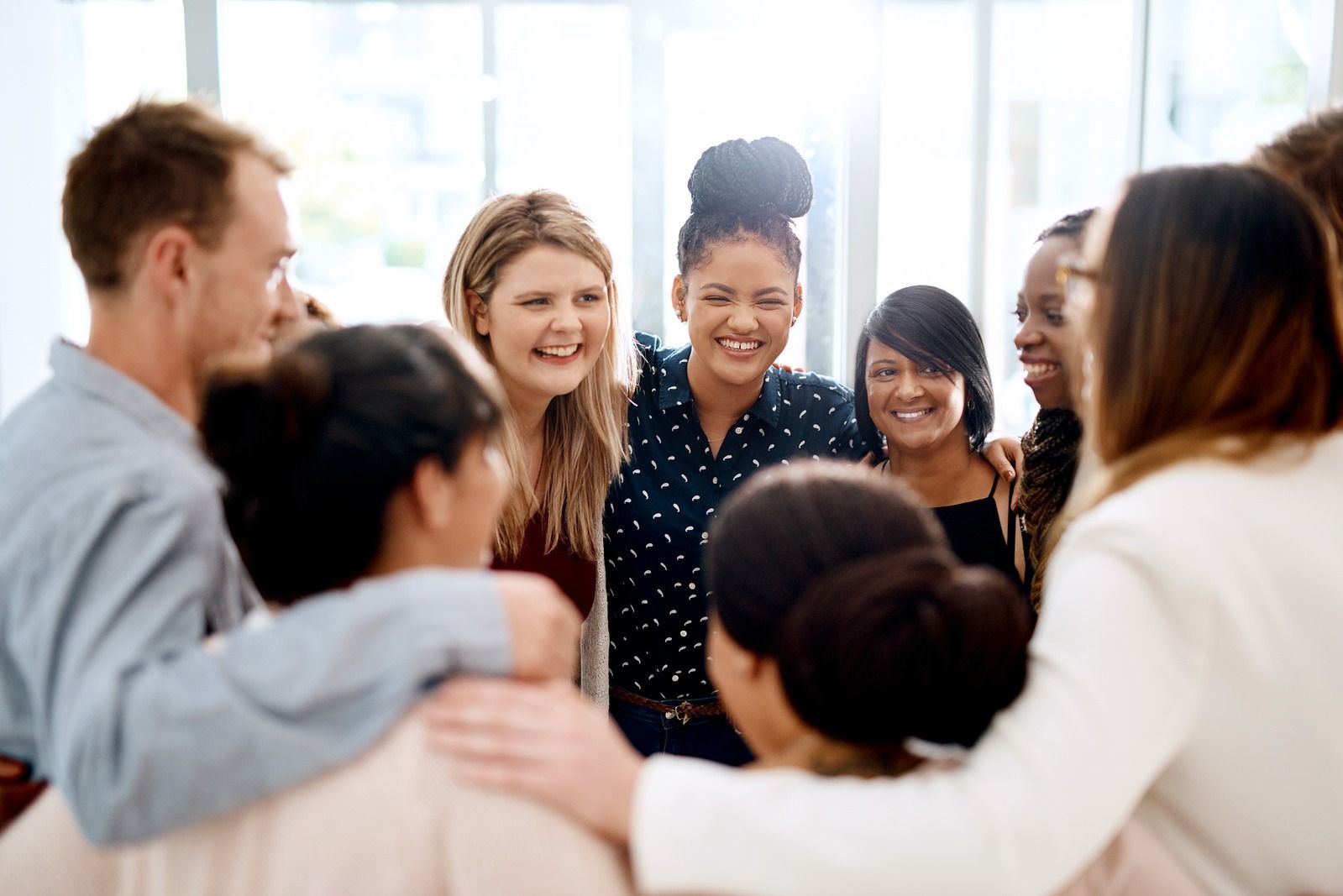 Group of people standing in a circle, smiling and chatting in a bright indoor setting