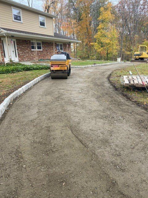Yellow utility truck on a curved gravel driveway beside a house in autumn.