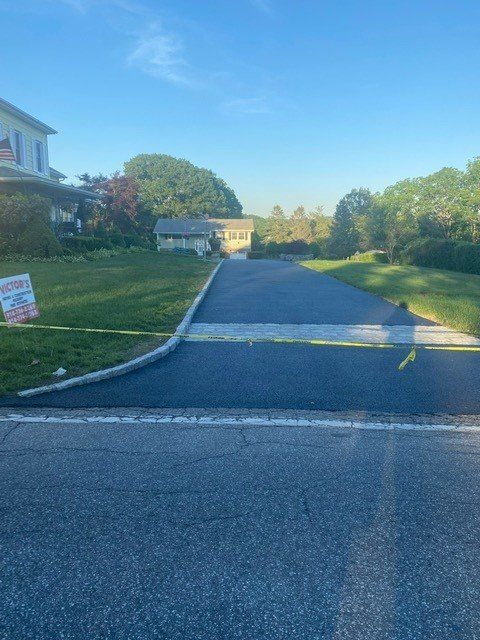 Residential driveway with a speed bump, lined by trees and a house in the distance under a clear blue sky
