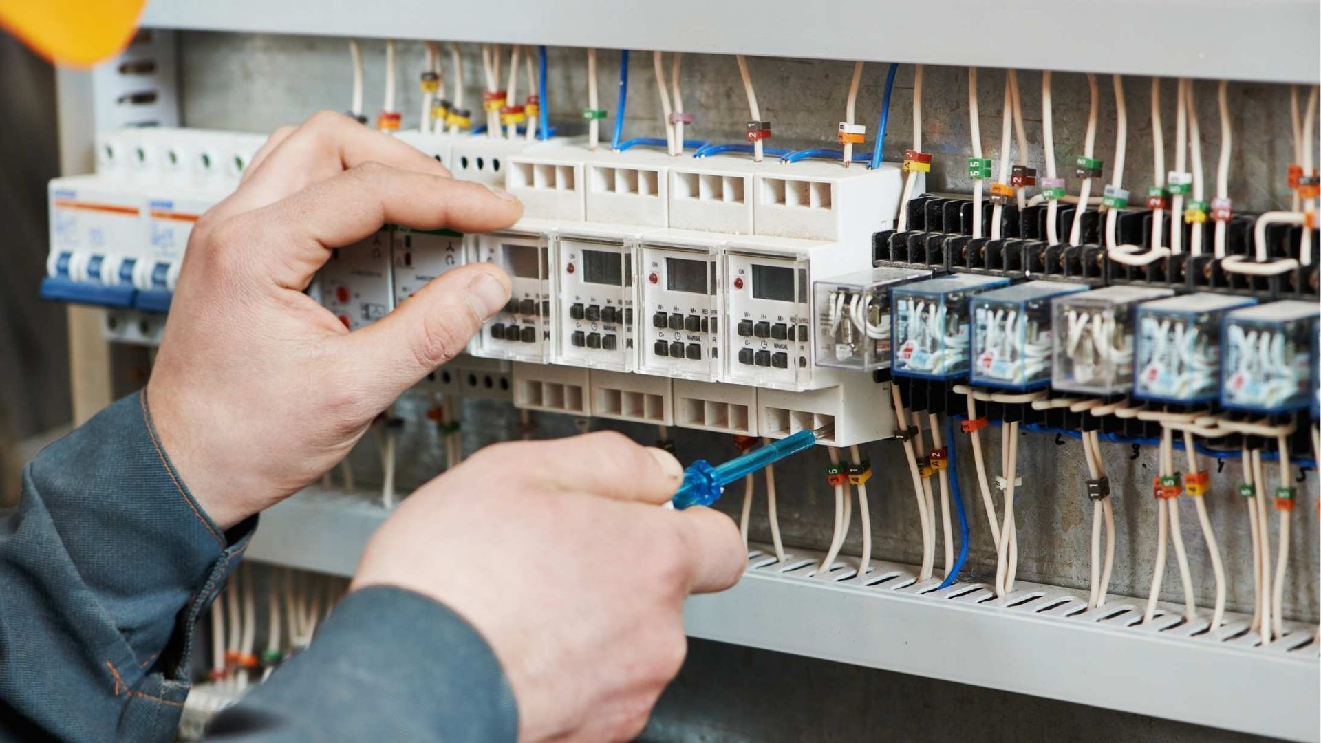 A man is working on an electrical panel with a screwdriver.