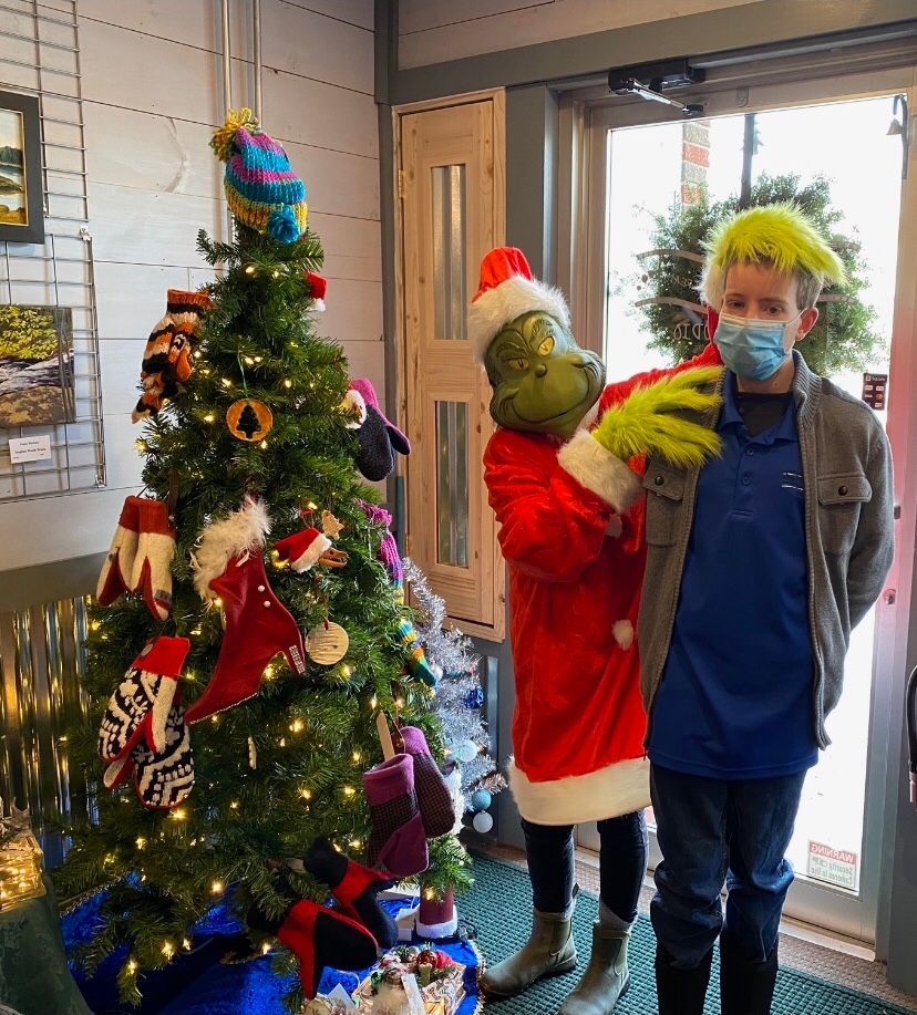A man in a mask is standing next to a grinch in front of a christmas tree.