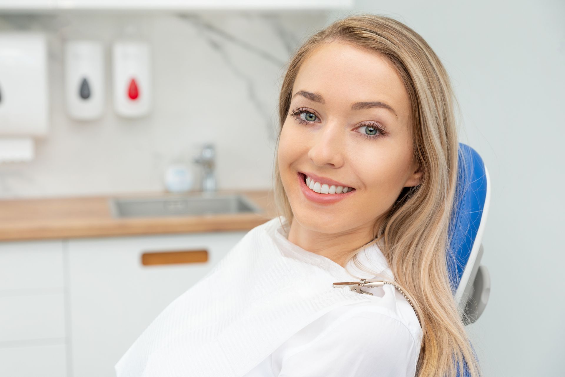 Woman smiles in a dental chair, white bib, clinic interior, blonde hair.