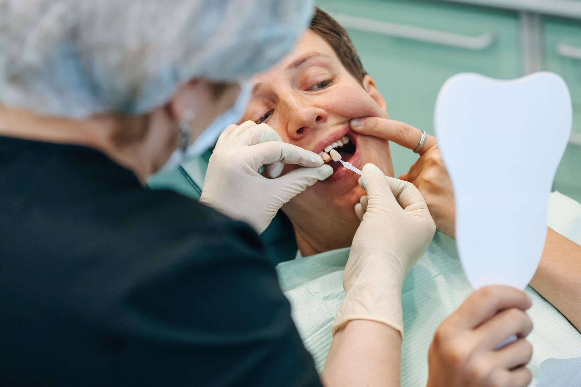 Dentist examining patient's teeth with color samples and a mirror in a dental office.