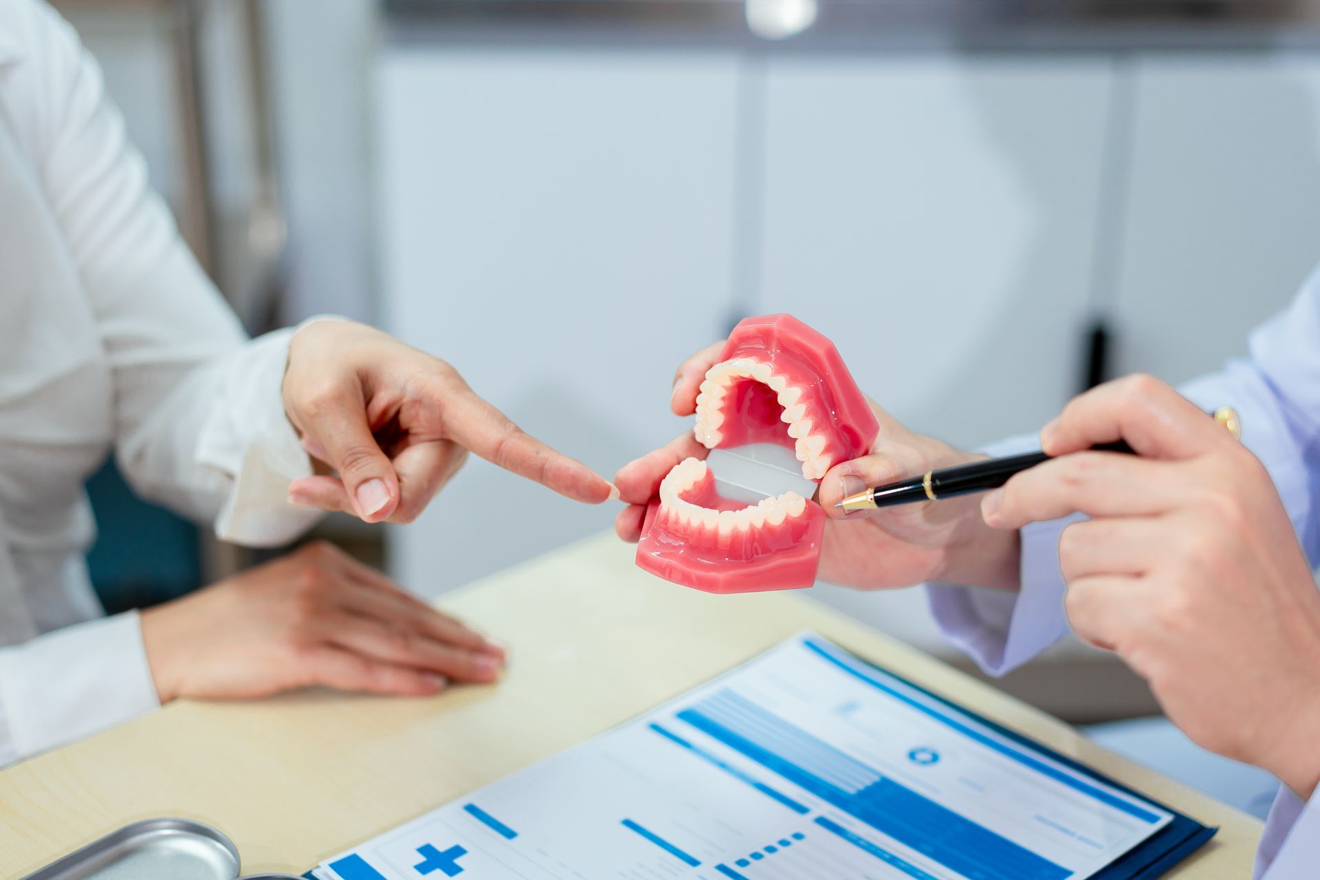 Dentist showing a patient a model of teeth, pointing at it with a pen.