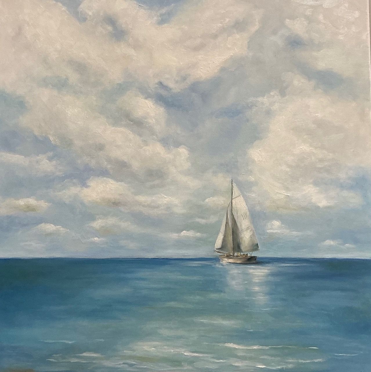 Sailboat on a calm blue sea beneath a cloudy sky, with a small distant horizon.