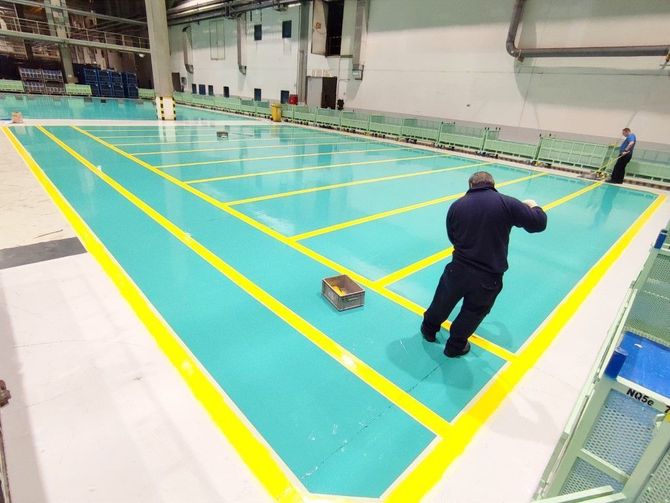 Indoor pool with turquoise water and yellow lane lines, with two people working near the edge.