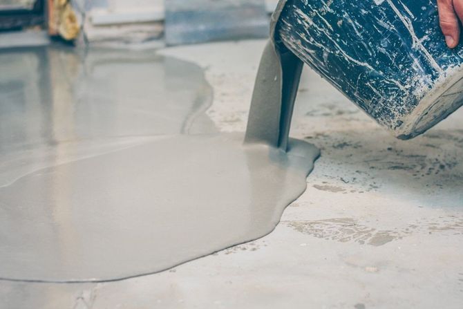 Blue paint bucket pouring white liquid onto a floor surface