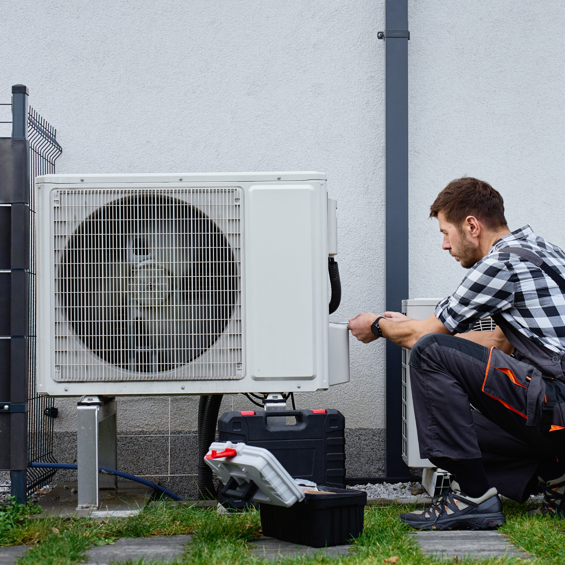 Technician servicing an outdoor AC unit; crouching with tools.
