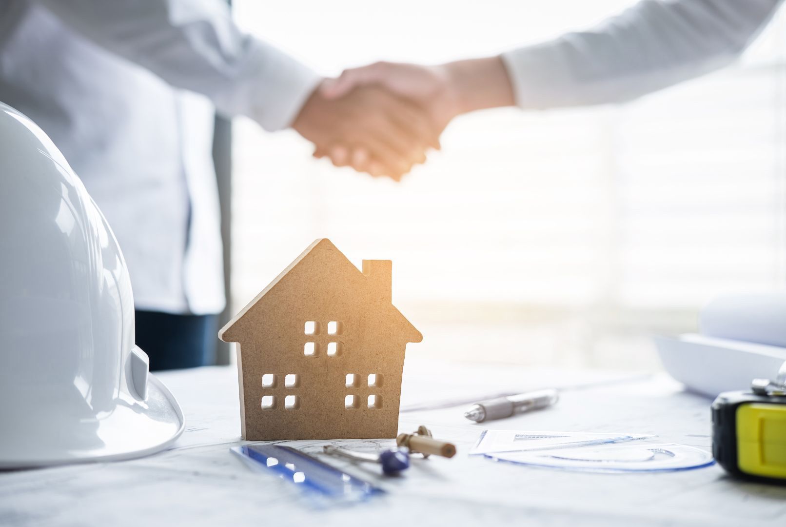 Two people are shaking hands over a model house on a table.