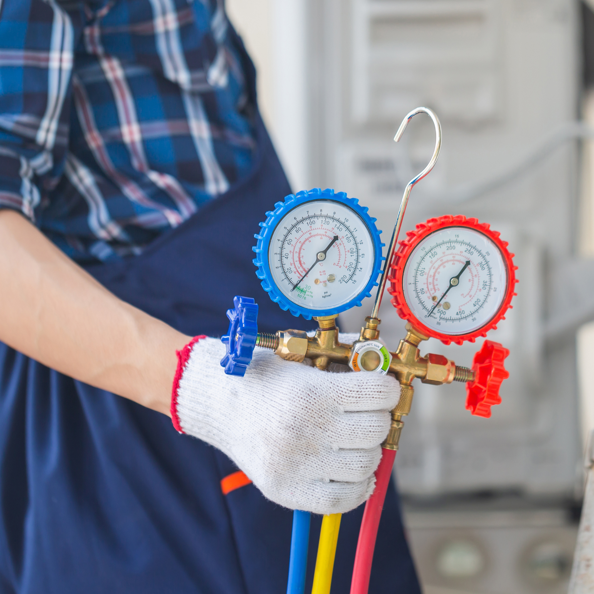 Person in blue and plaid holding HVAC gauges. White glove, red and blue gauges.