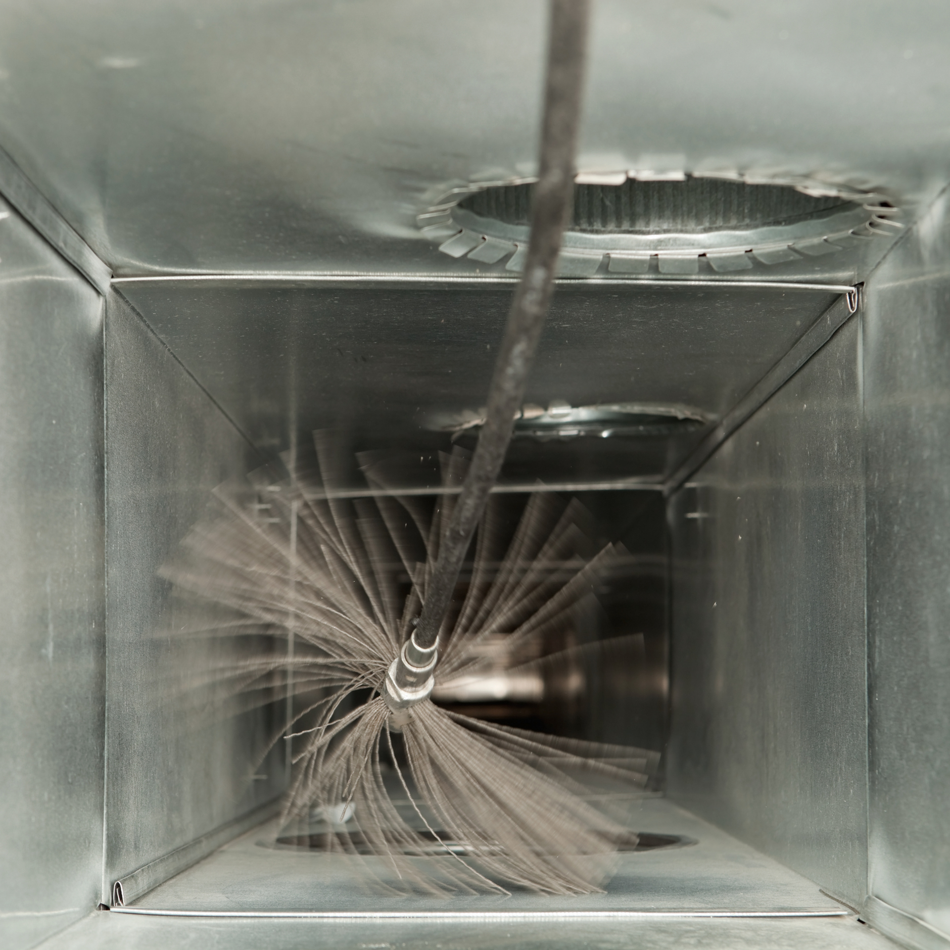 A duct cleaning brush inside a dusty, metal air duct, cleaning the interior.