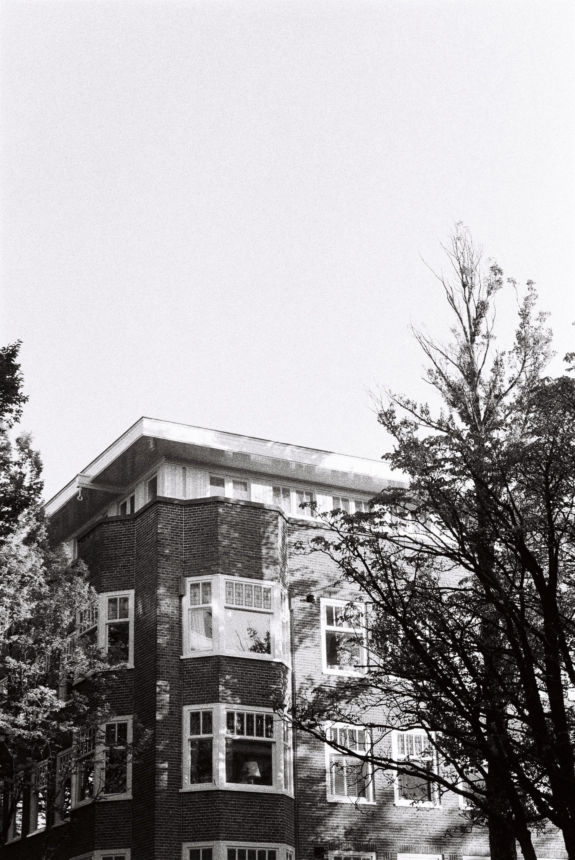Black-and-white view of a brick building with bare trees against a bright sky