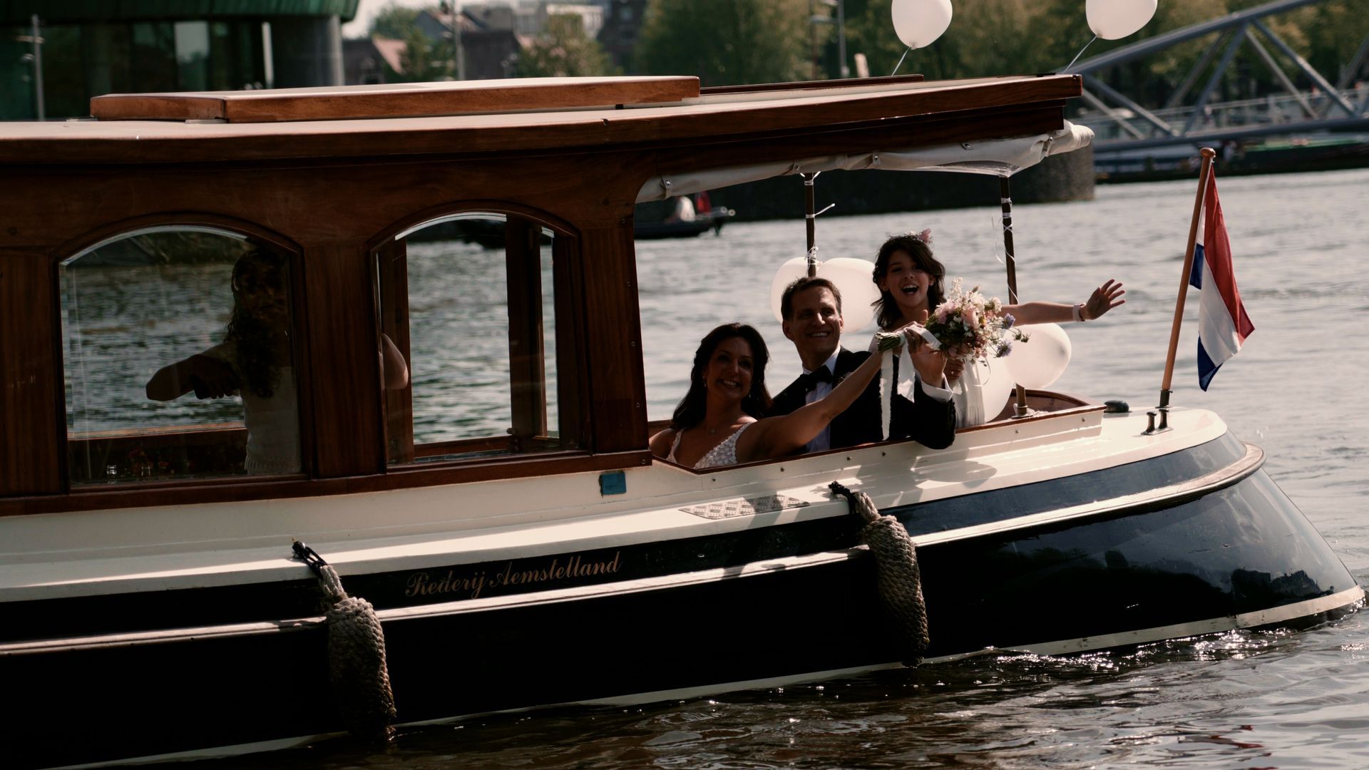 People on a small wooden boat cruising on the water, with a cabin and flag visible.