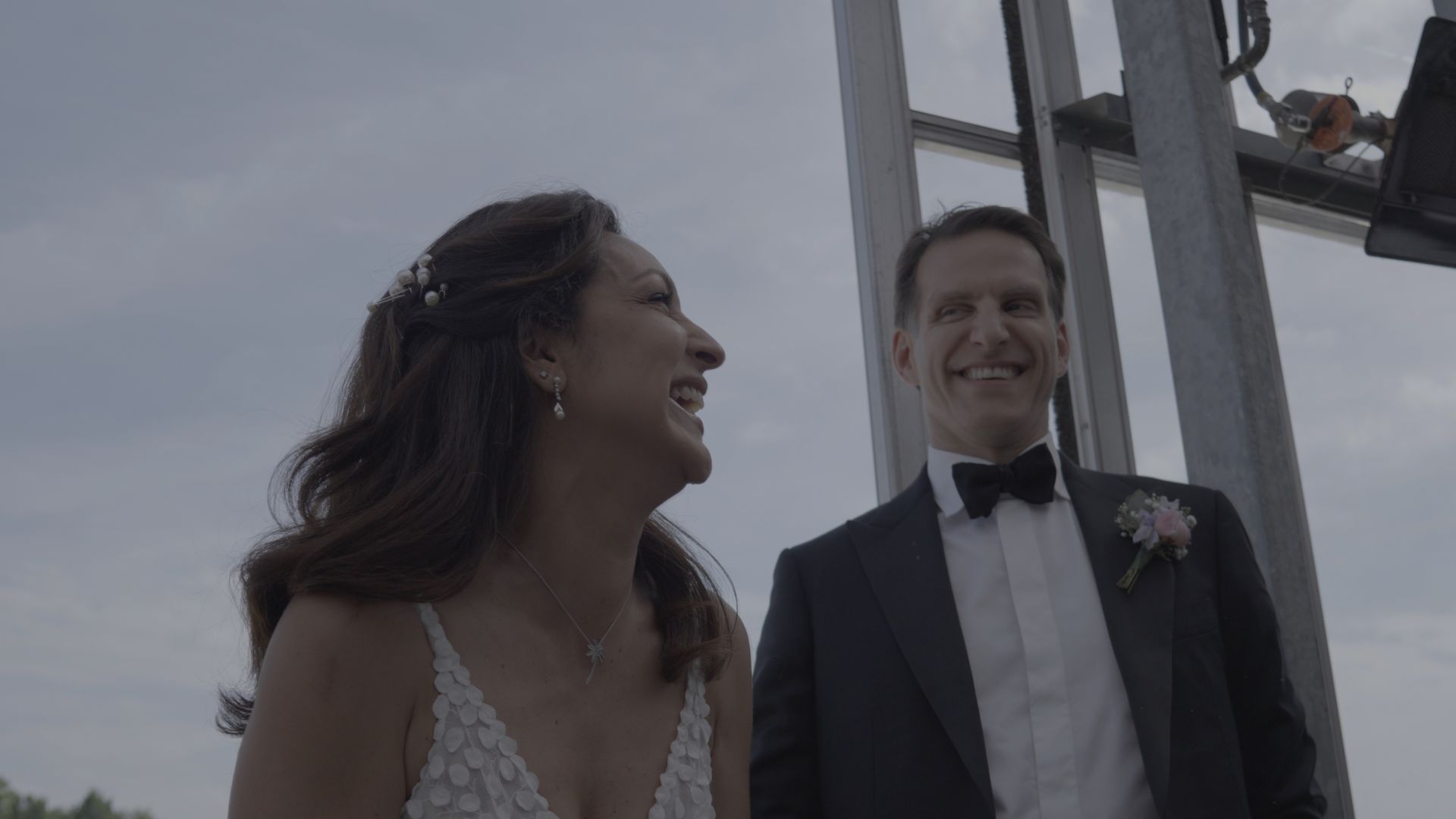 Bride and groom smiling at an outdoor wedding ceremony near metal beams at dusk