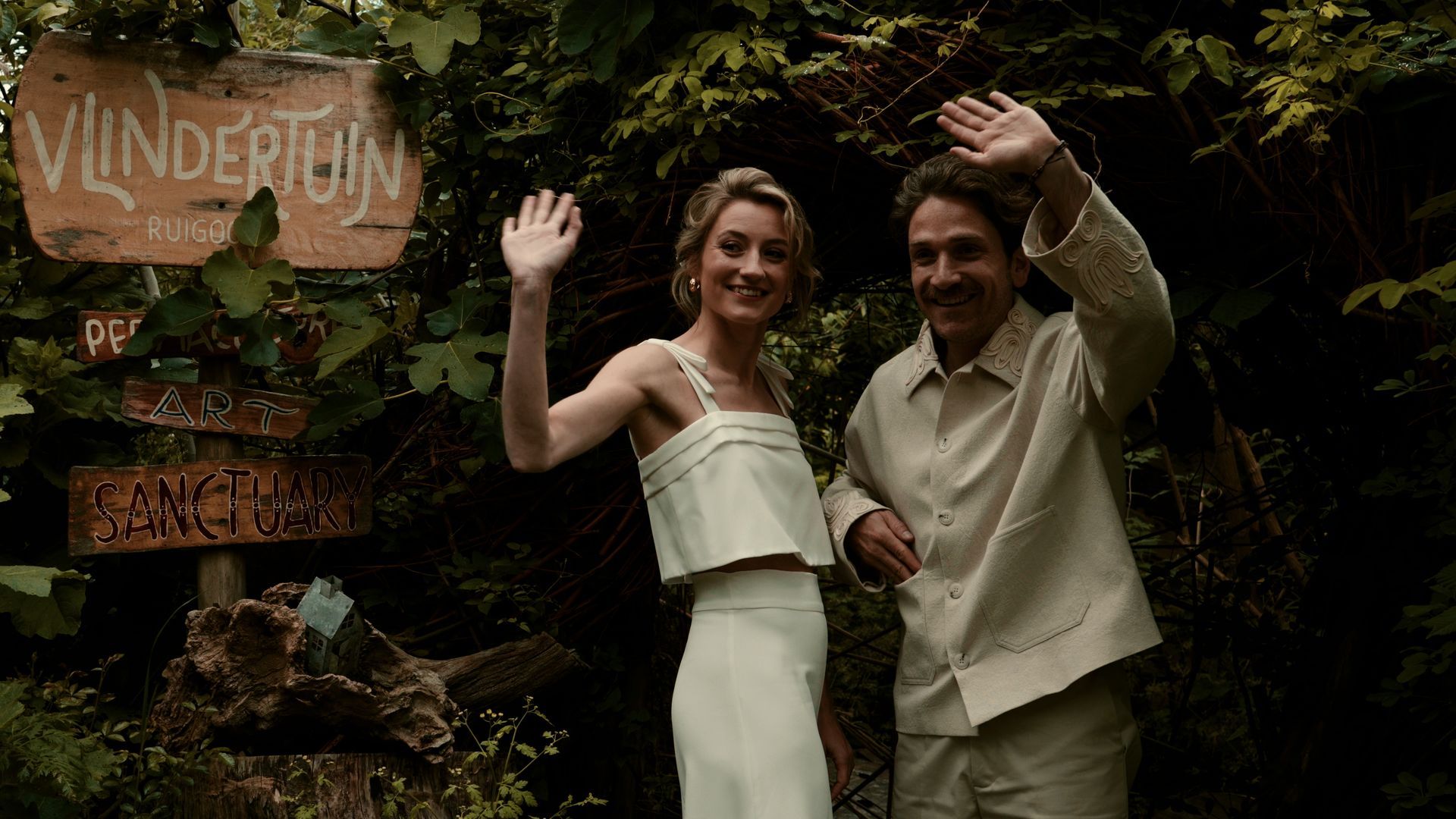 Two people waving beside a rustic 