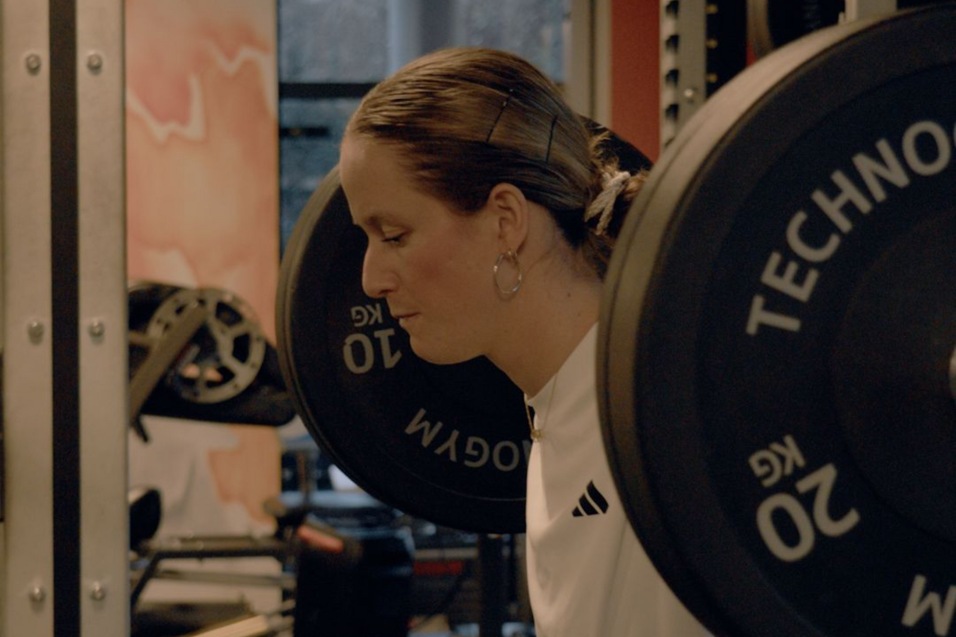 Woman lifting a barbell in a gym, close-up side view with weight plates visible