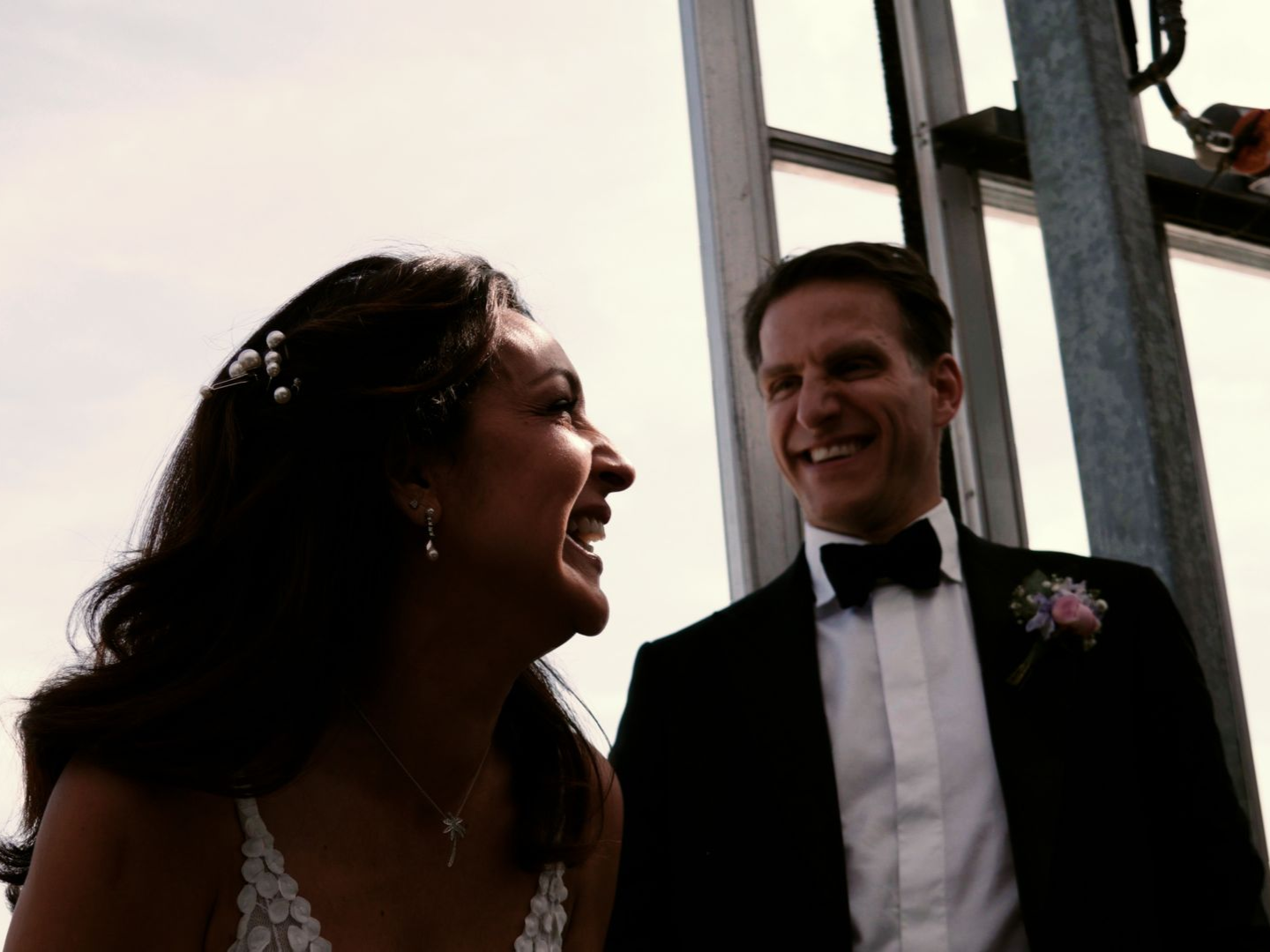 Bride and groom smiling at each other outdoors by a building entrance