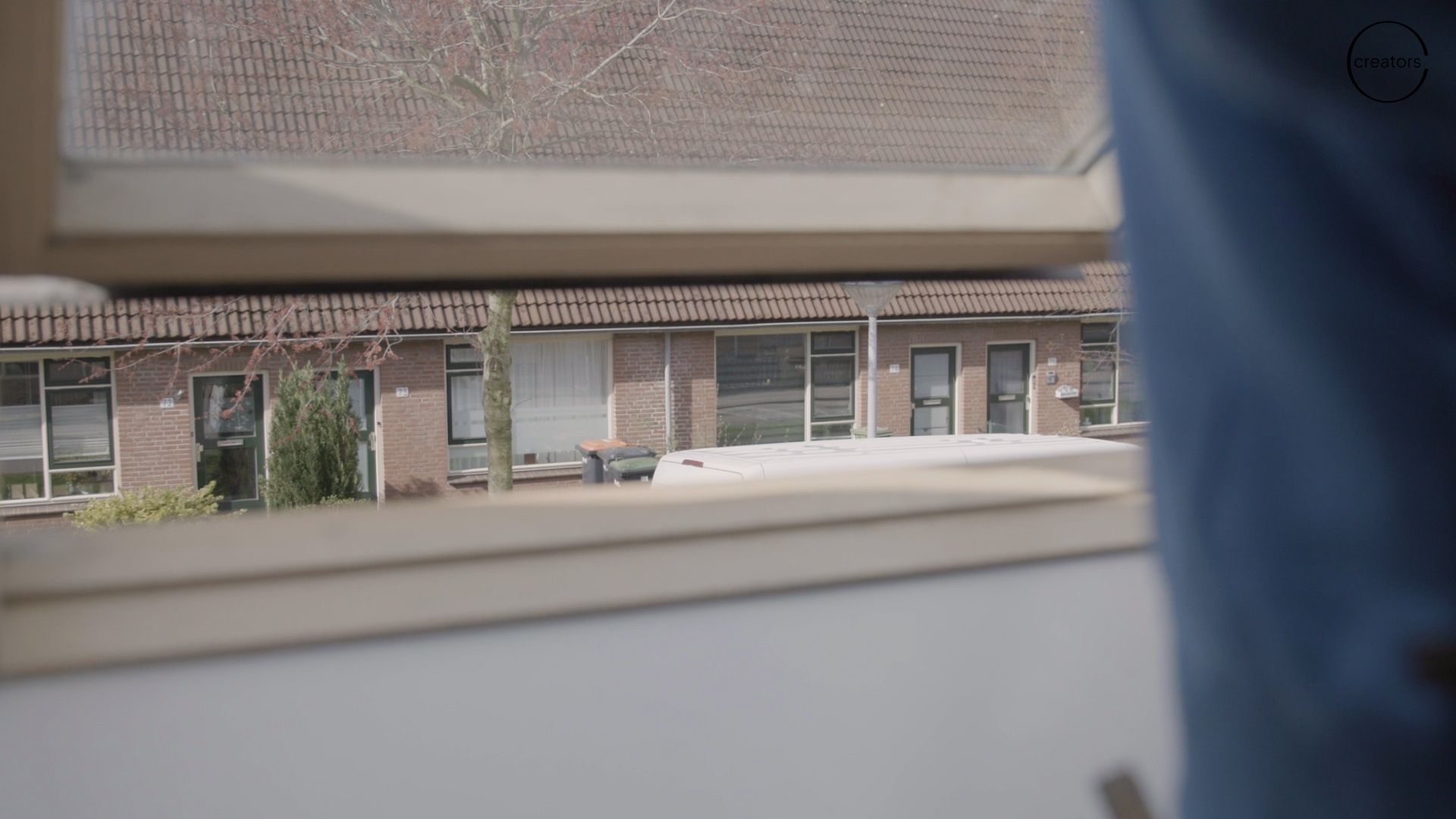 View from inside a room through a window, showing a row of brick houses and a blue curtain on the right.