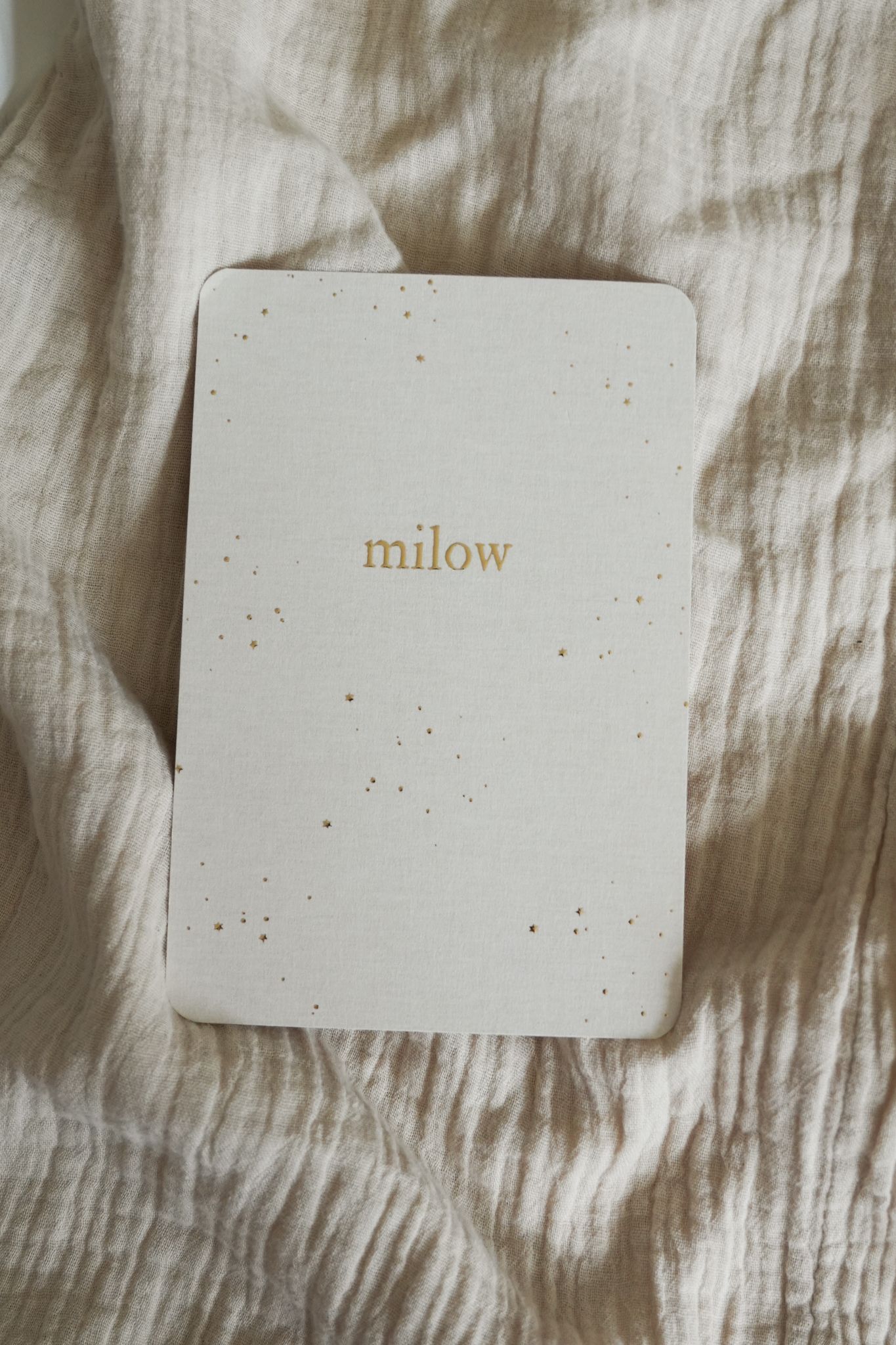 Small white speckled card with the word “milow” on a beige fabric background.