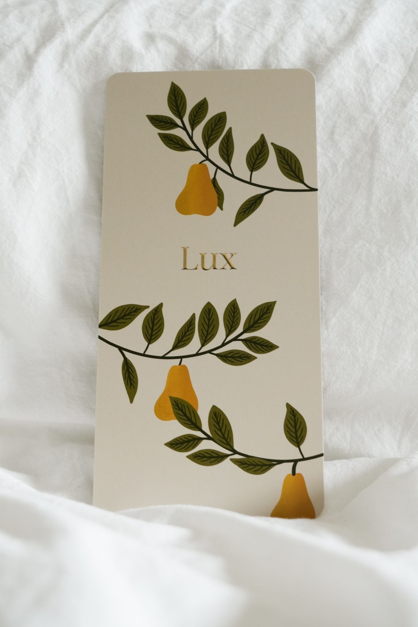 Beige card with green leaves, yellow pears, and the word “Lux” on a white fabric background