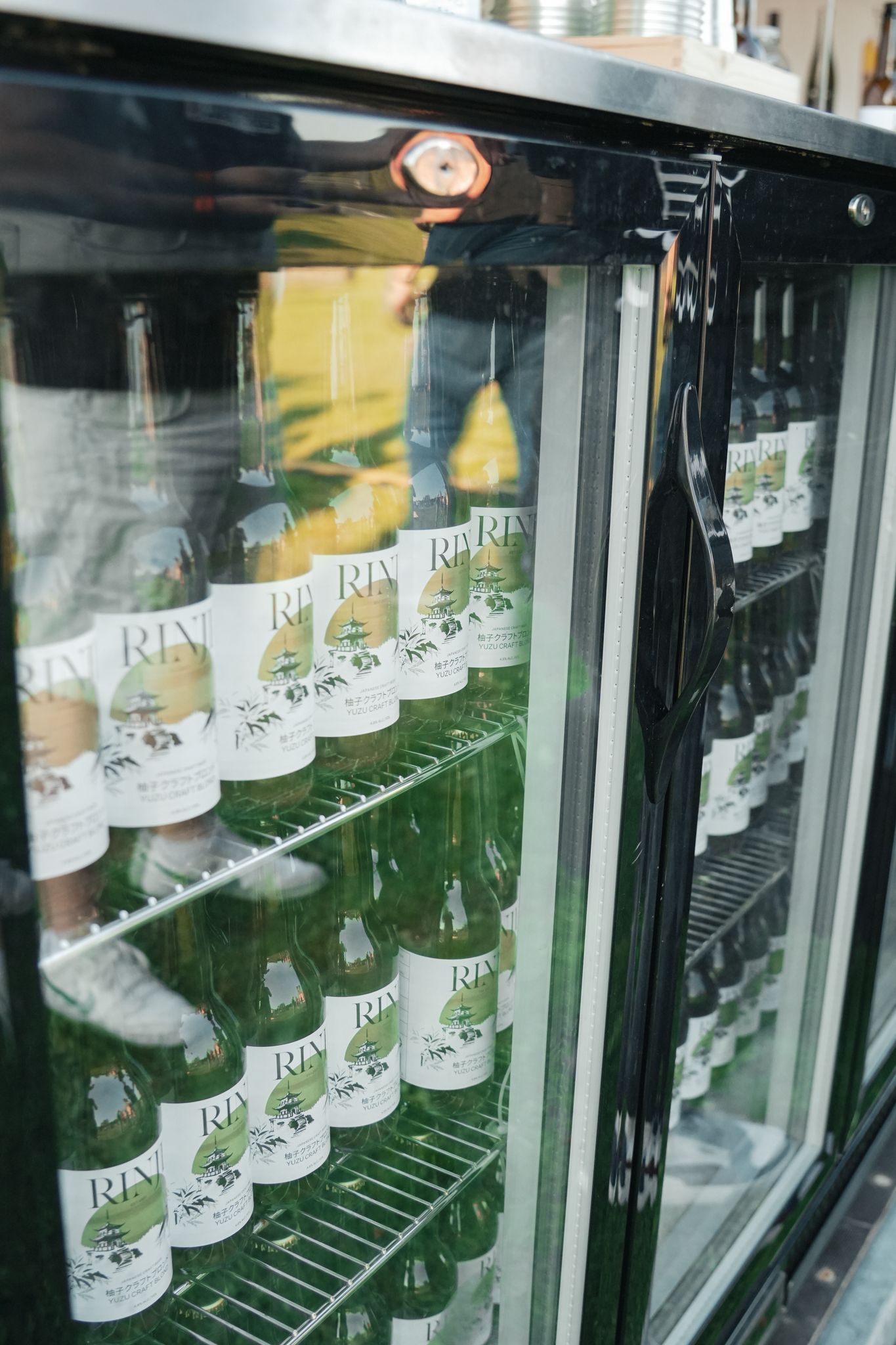 Refrigerated display case with rows of bottled drinks on shelves and a glass door partly open