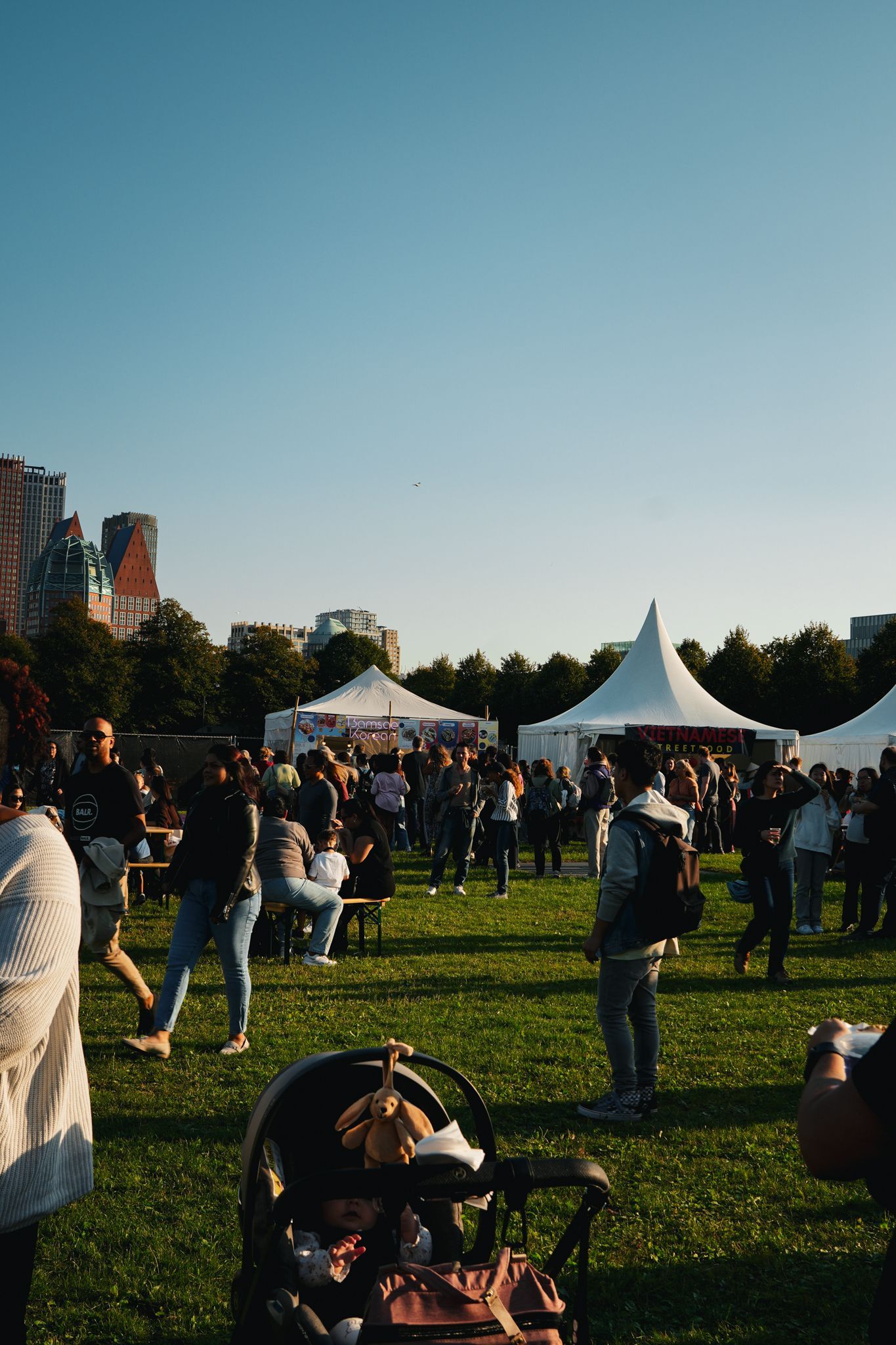 People gathered on a grassy field at an outdoor festival with white tents at sunset.