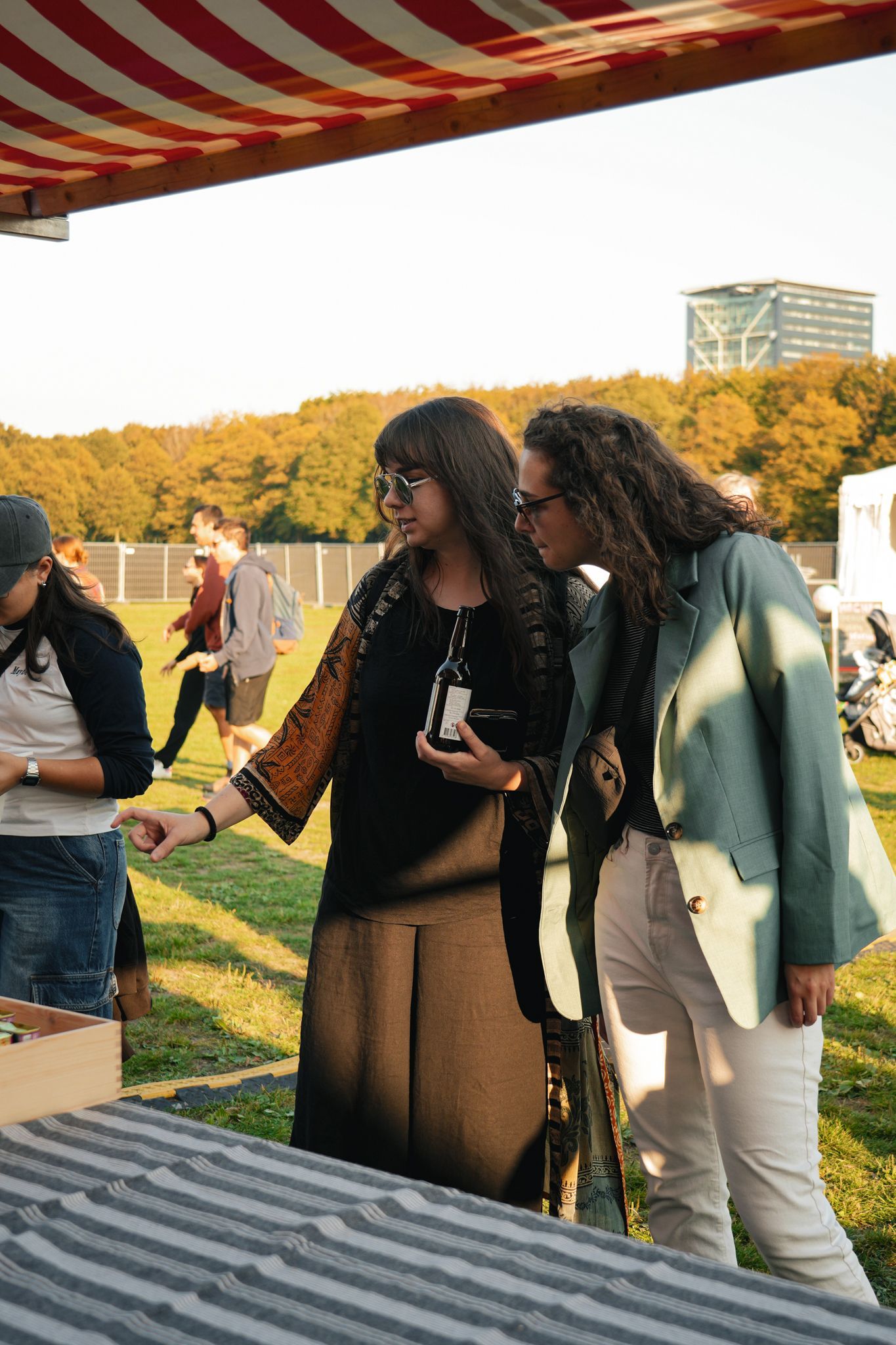 Two women outdoors at a picnic table, leaning over and looking at items on the table.