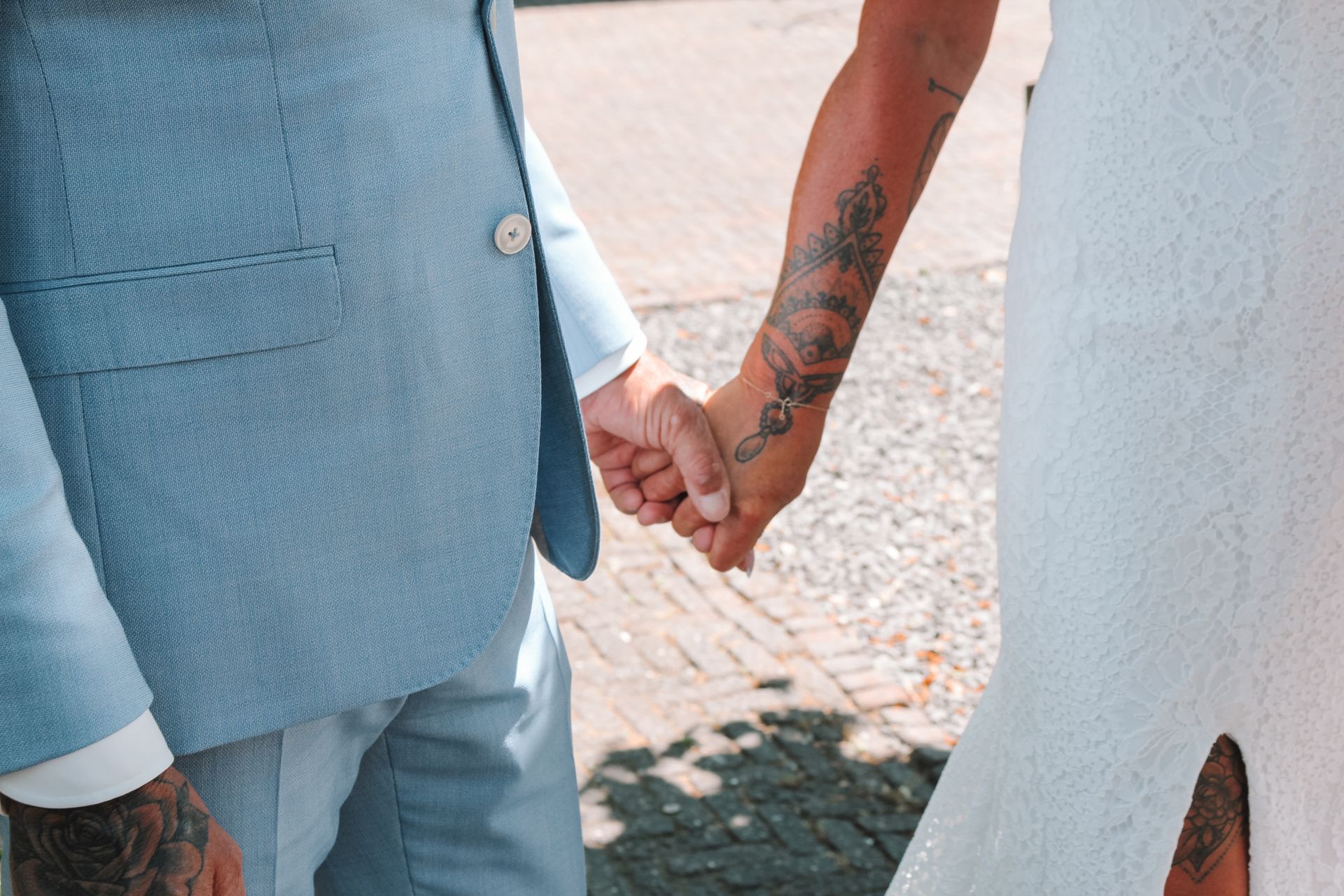 Two people in light blue attire holding hands outdoors by a white wall.