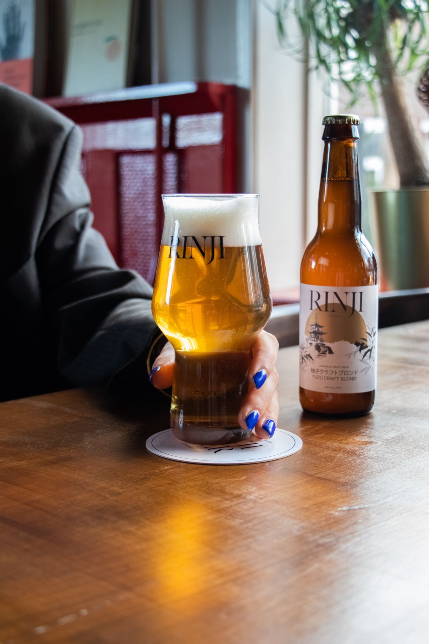 Beer glass and bottle on a wooden table beside a seated person in a restaurant