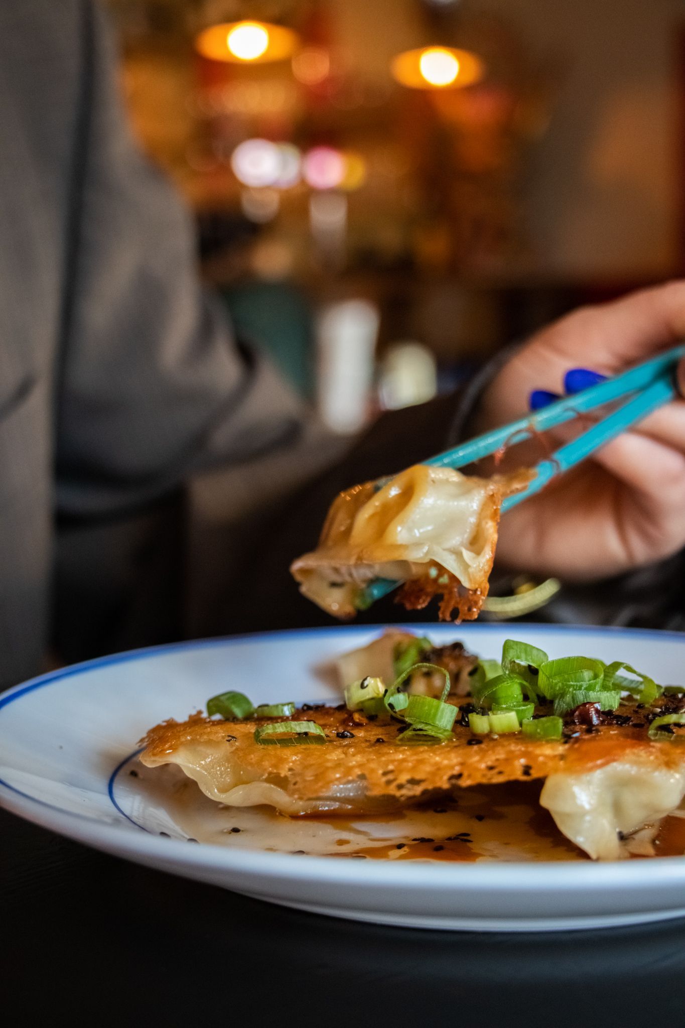 Hand holding blue chopsticks above a plated fish dish in a dimly lit restaurant