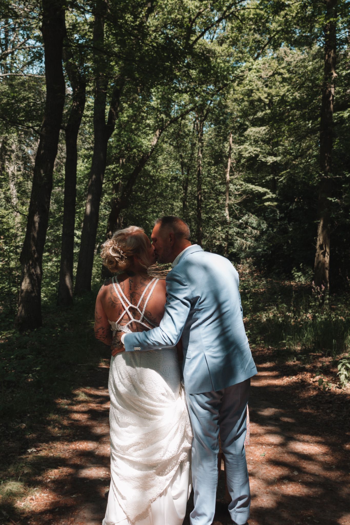 Couple in formal attire kissing on a sunlit forest path