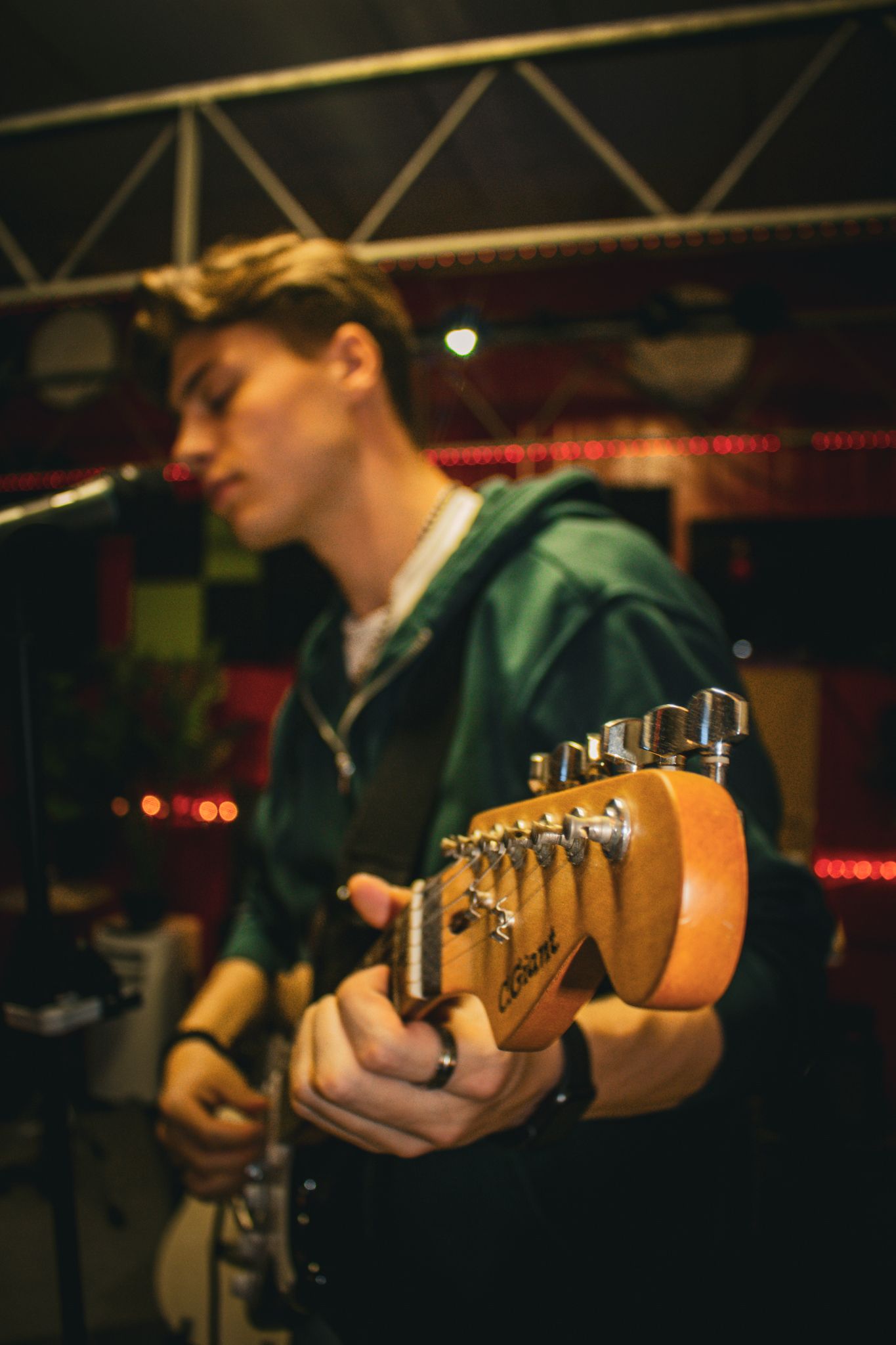 Musician playing electric guitar on a dimly lit stage, with blurred lights in the background