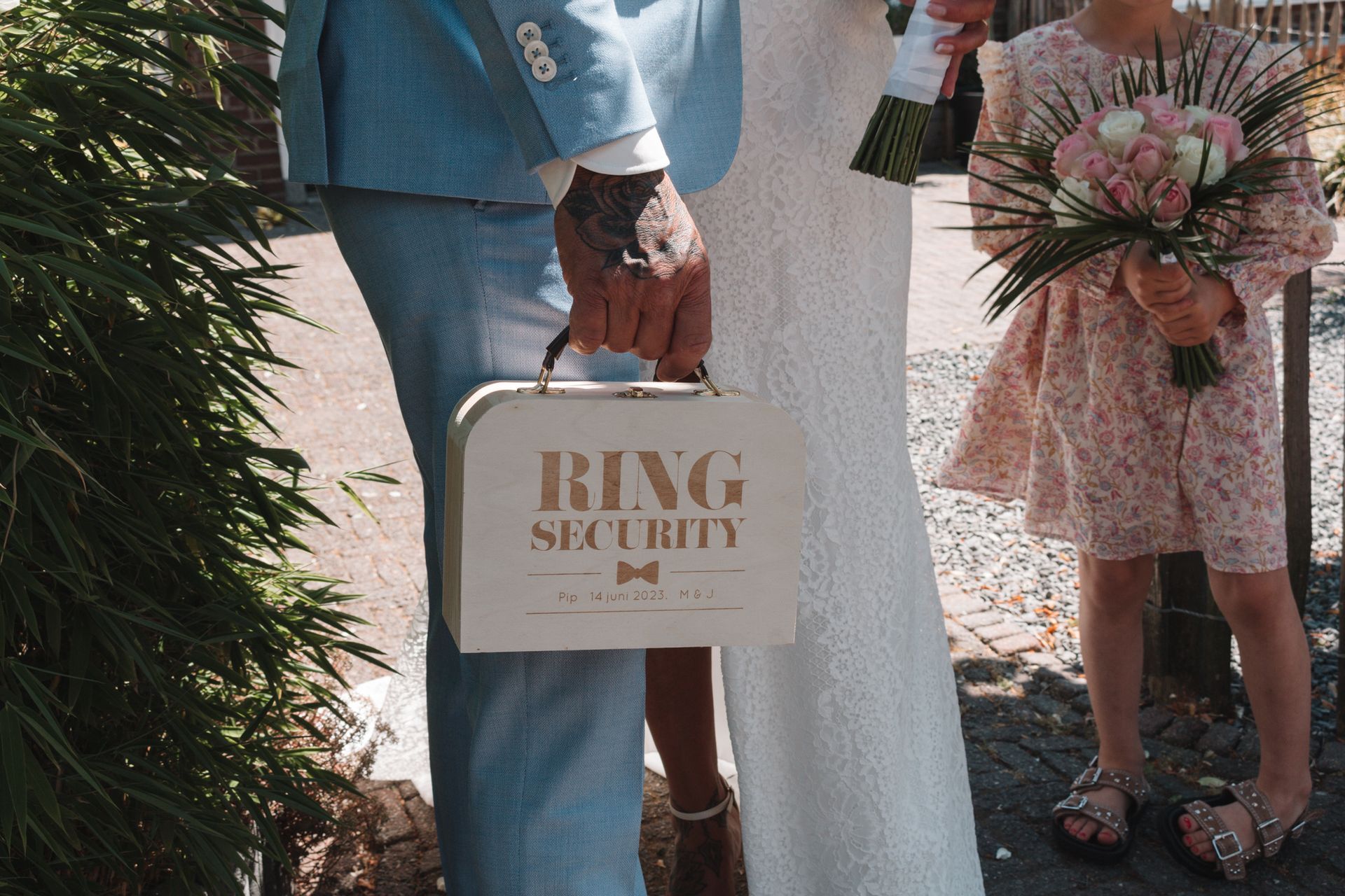 People holding wedding flowers and a sign reading “BIG SMILE” outdoors in formal attire