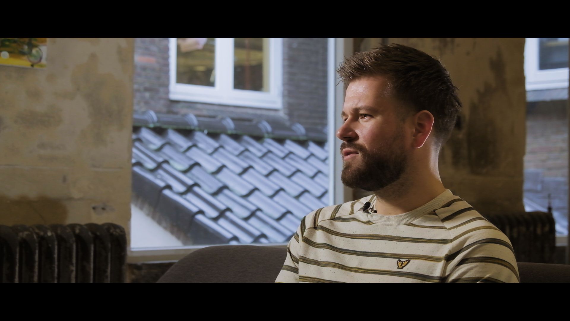 Man sitting indoors by a window, looking to the right in a striped shirt.