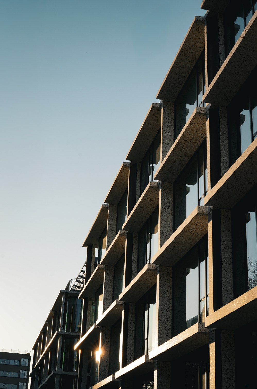 Modern building facade with repeating balconies, seen from below against a blue sky