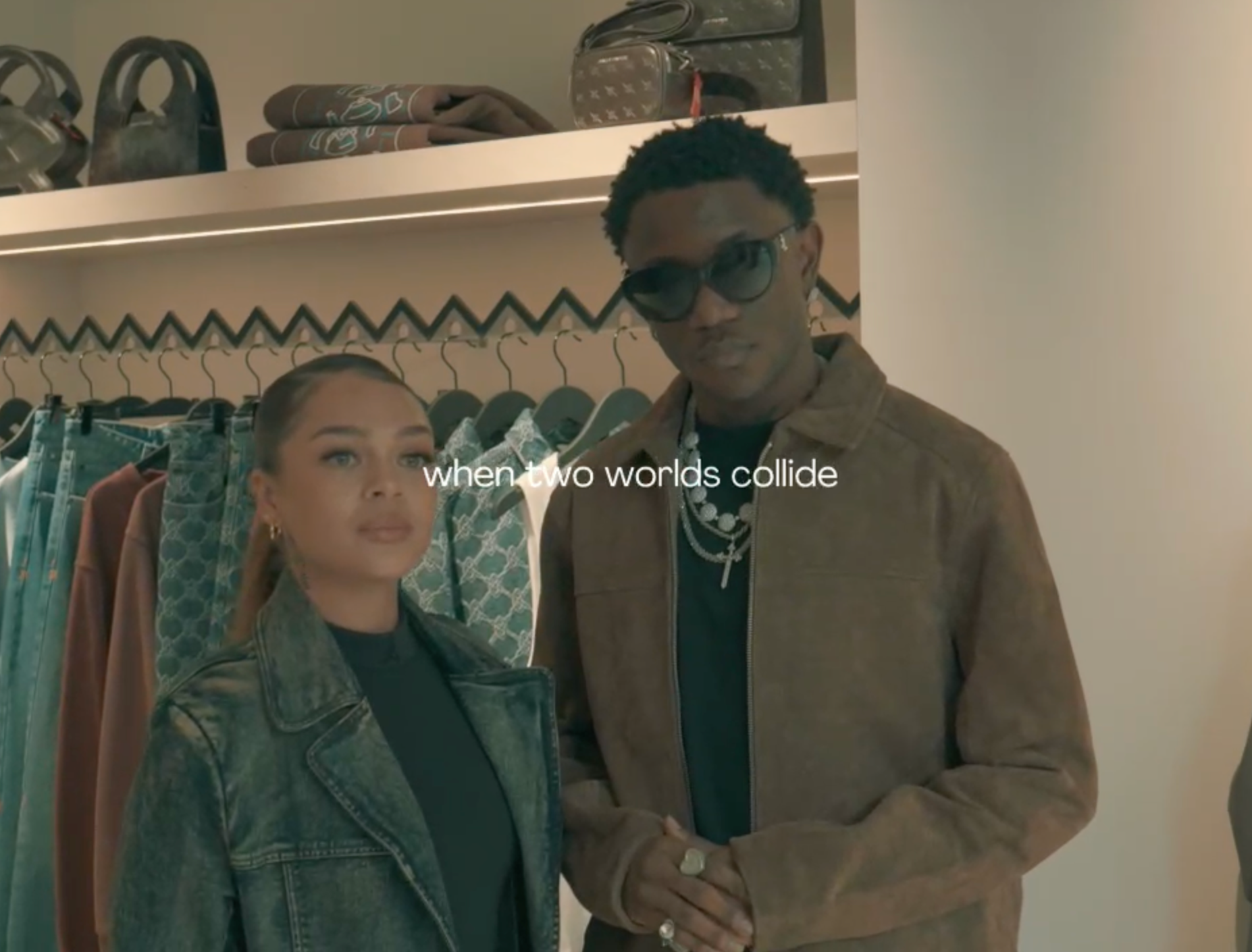 Two people standing in a clothing store, wearing jackets and sunglasses, with clothes racks behind them