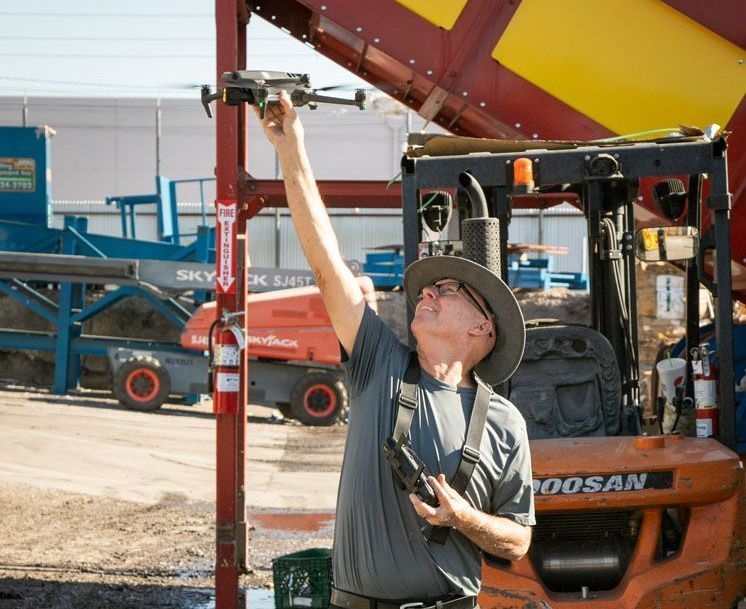 Robert Biggs, Professional Drone Photographer A man holding a drone in front of a doosan forklift