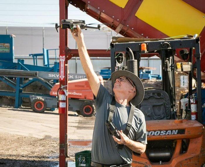 A man is using a drone in front of a Photo by Phoenix Drone Pros, Robert Biggs, forklift