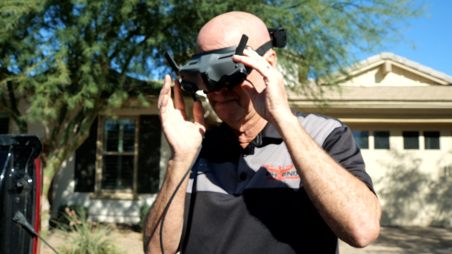Man adjusting virtual reality goggles outdoors, in front of a house.