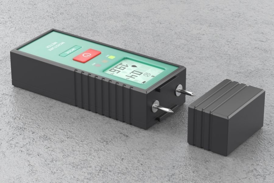 Pin-type moisture meter with its protective cap removed and steel probes exposed, resting on a gray concrete surface