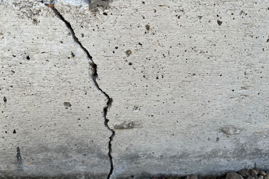 Close-up of a jagged crack running through a weathered concrete foundation edge