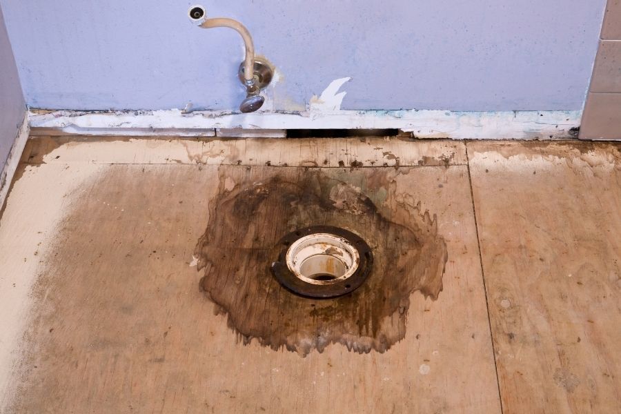 Swollen baseboard and stained flooring beside a bathtub caused by a hidden bathroom leak in a St. Petersburg home