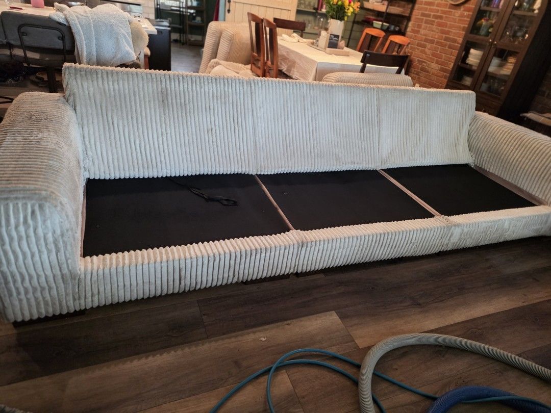Sofa deck exposed with all cushions removed to reach seams and crevices during cleaning prep