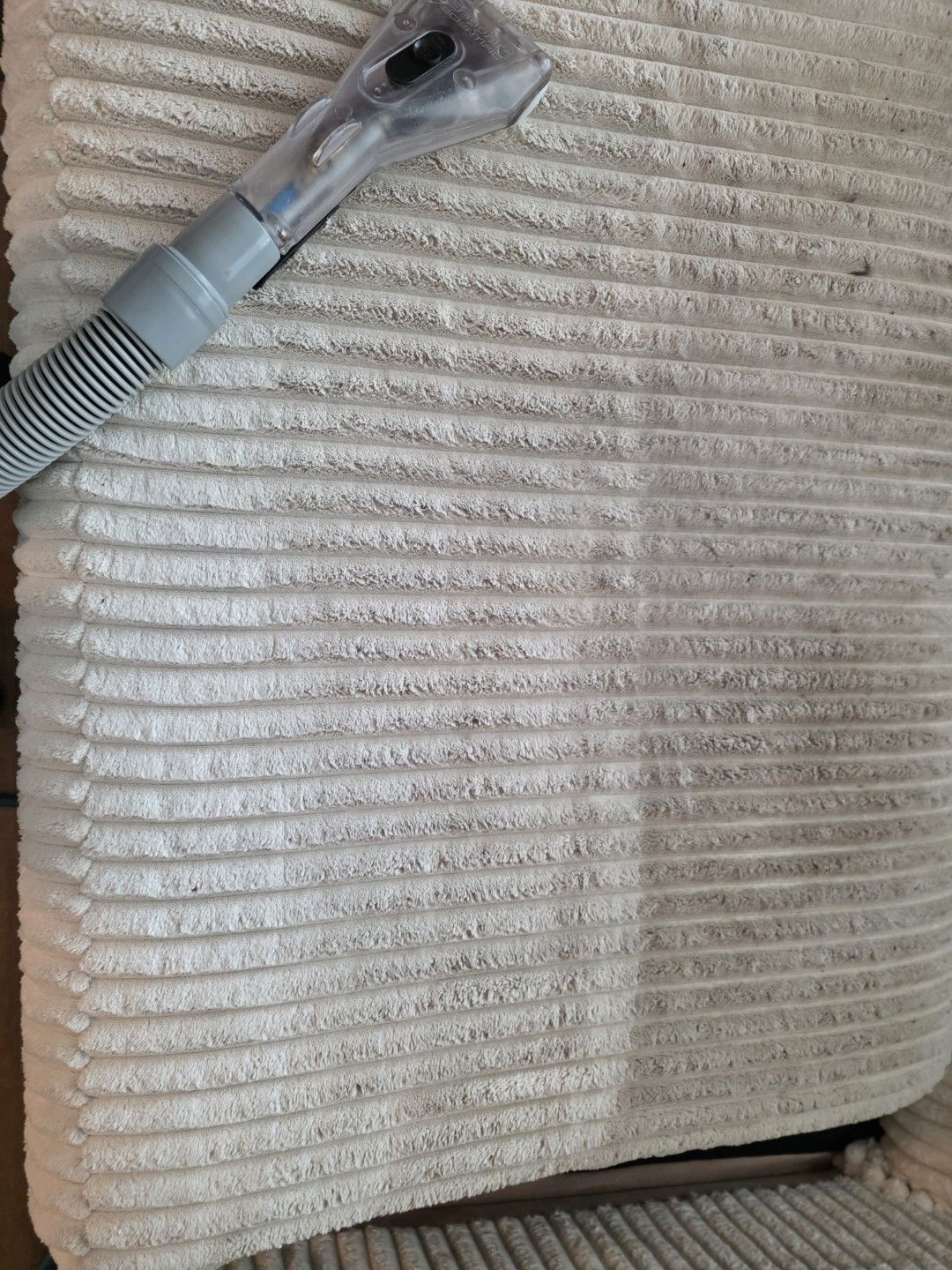 Upholstery cleaning wand mid pass showing the clean half of a sofa cushion against the soiled half