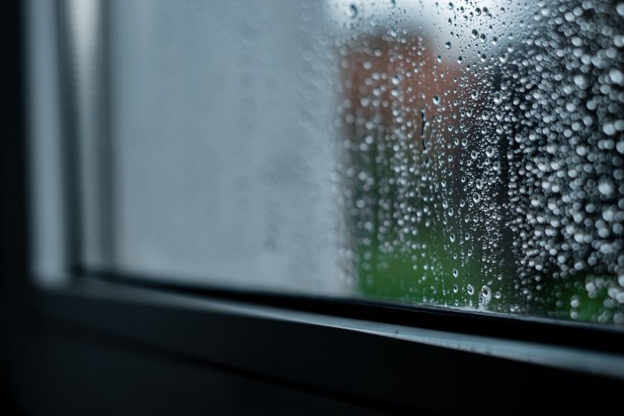 Rainwater running down a window pane during a heavy storm with a blurred green yard outside
